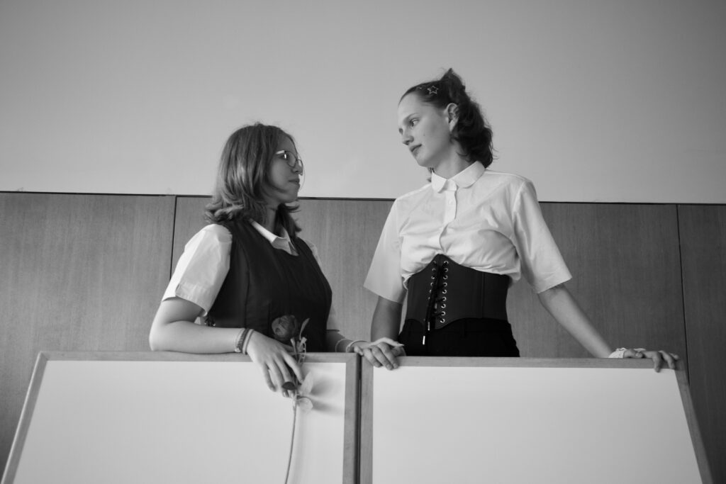 Two women in vintage-inspired outfits converse at a whiteboard in a modern setting.